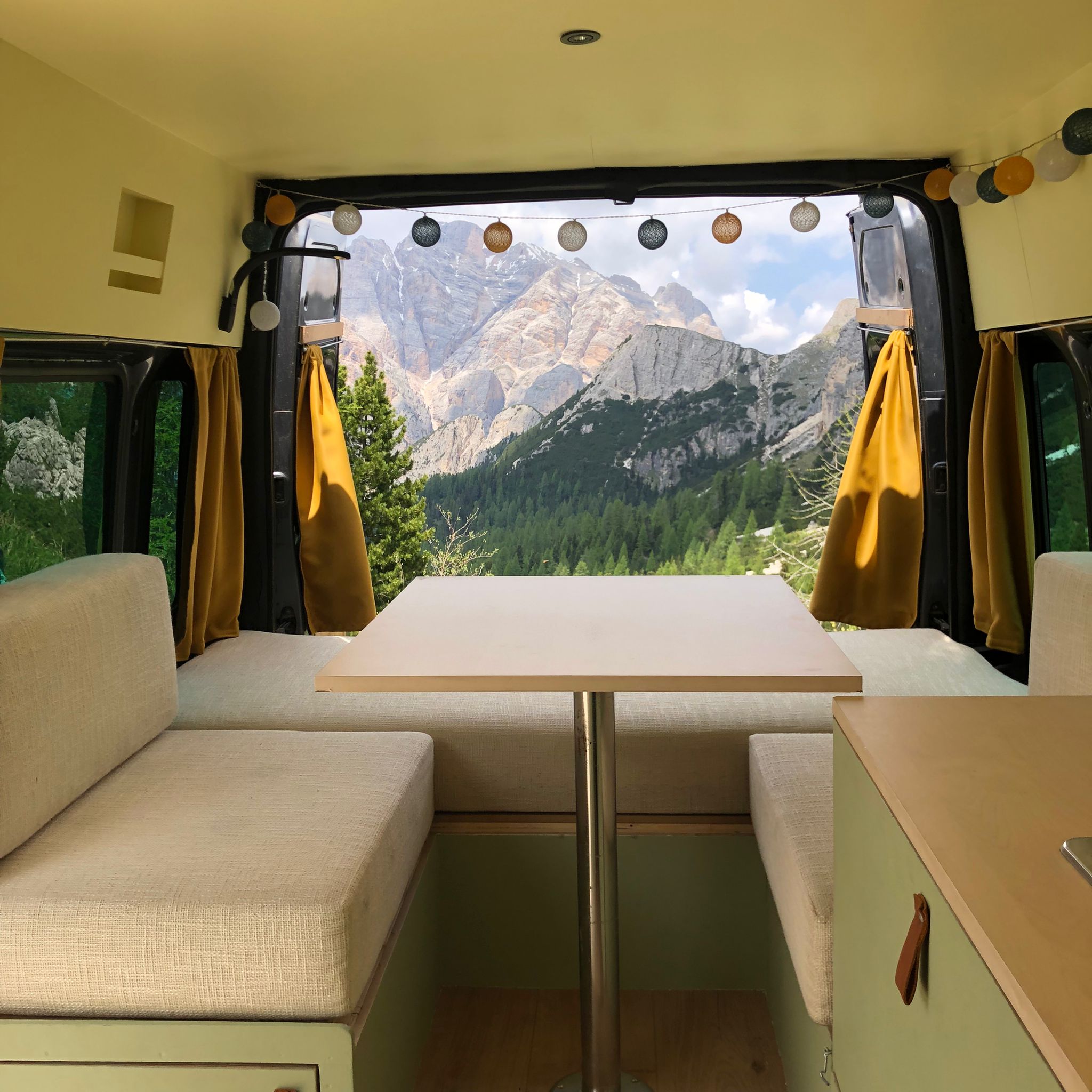 Binnenkant van een caravan, tafel met 2 bankjes, uitzicht op de bergen